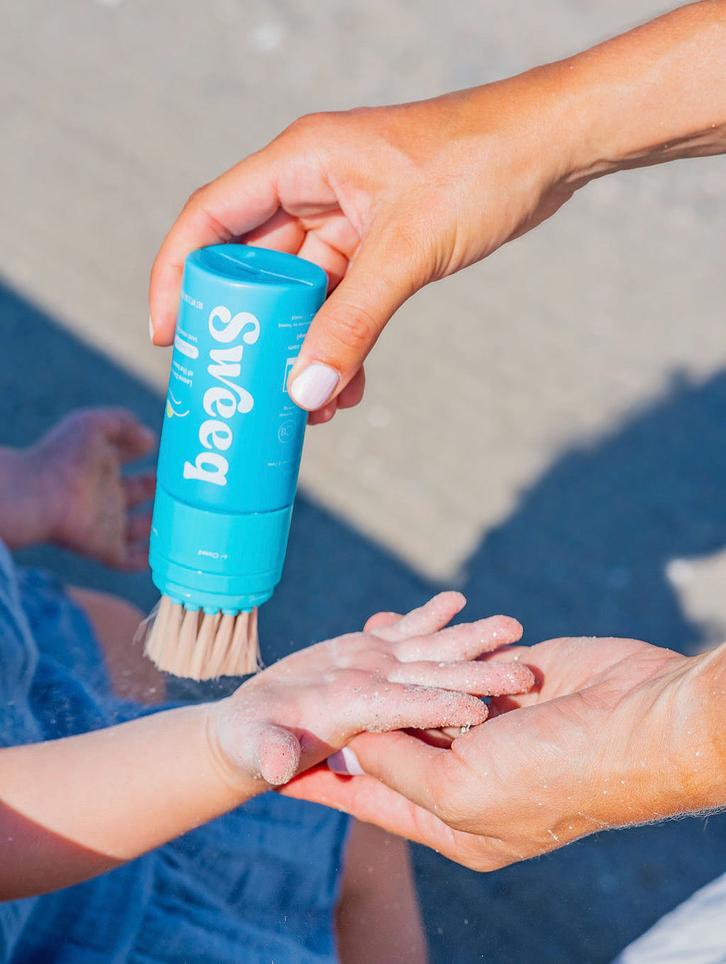 Mom brushing sand off child’s hand with Sweeq to show soft bristles and powder